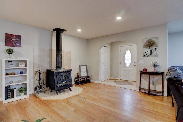 entrance foyer with arched walkways, light wood-type flooring, a wood stove, and recessed lighting