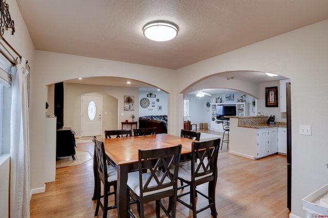 dining area featuring arched walkways, light wood finished floors, and a wealth of natural light