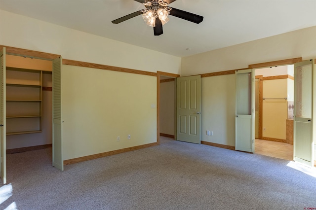 unfurnished bedroom featuring a walk in closet, ensuite bathroom, a ceiling fan, light carpet, and baseboards