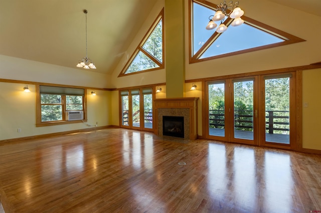 unfurnished living room with a chandelier, high vaulted ceiling, wood finished floors, and baseboards