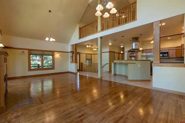 unfurnished living room featuring an inviting chandelier, baseboards, high vaulted ceiling, and light wood finished floors