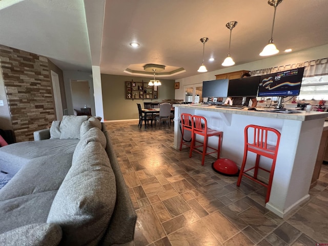 interior space featuring baseboards, a raised ceiling, a kitchen breakfast bar, decorative light fixtures, and open floor plan