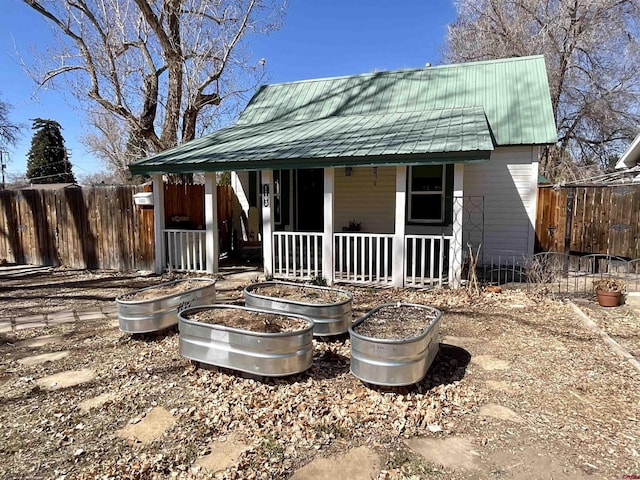 rear view of house featuring covered porch, metal roof, and fence