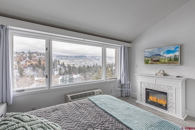 bedroom featuring a wall mounted AC, wood finished floors, a tile fireplace, and vaulted ceiling