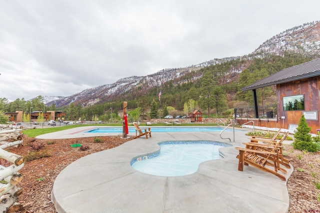 community pool with a mountain view, a patio, and a view of trees