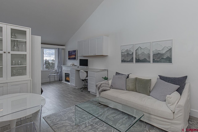 living area featuring baseboards, high vaulted ceiling, a warm lit fireplace, and wood finished floors