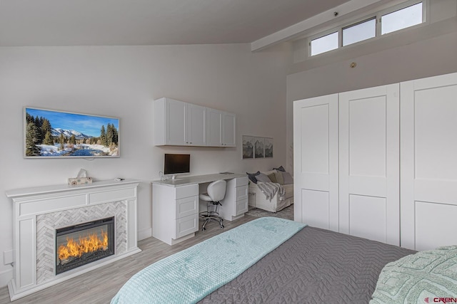 bedroom with high vaulted ceiling, light wood-style flooring, and a tiled fireplace