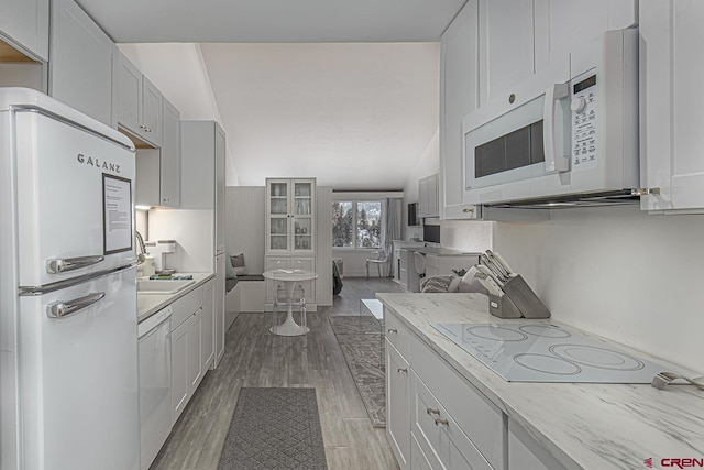 kitchen featuring light wood-type flooring, white appliances, white cabinets, and vaulted ceiling