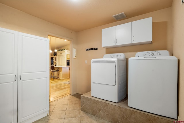 washroom featuring washer and clothes dryer, light tile patterned floors, cabinet space, and visible vents