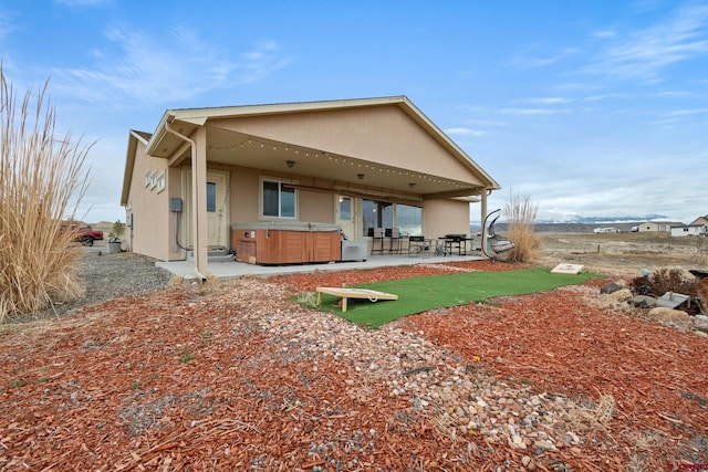 back of property featuring stucco siding, a patio area, and a hot tub