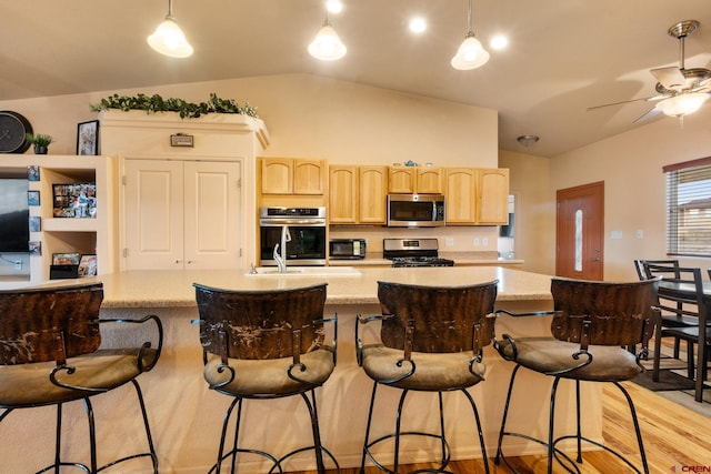 kitchen featuring light wood finished floors, a toaster, light brown cabinetry, vaulted ceiling, and appliances with stainless steel finishes