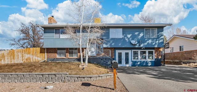 view of front of property featuring fence, driveway, a chimney, french doors, and brick siding