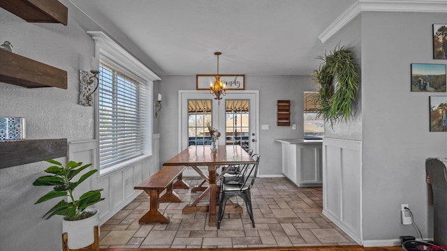 dining area with baseboards, ornamental molding, french doors, stone finish flooring, and a notable chandelier