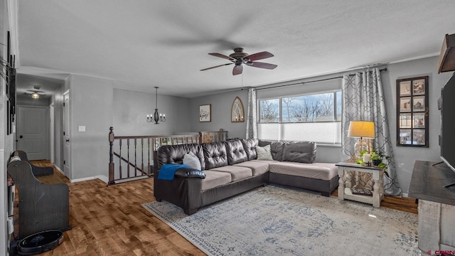 living area featuring ceiling fan with notable chandelier, a textured ceiling, baseboards, and wood finished floors