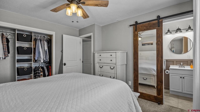 bedroom featuring ceiling fan, a barn door, light carpet, a closet, and a sink