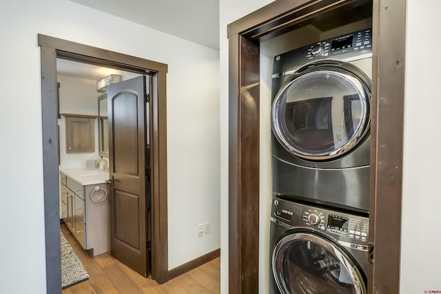 clothes washing area featuring stacked washer and dryer, a sink, light wood finished floors, baseboards, and laundry area