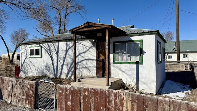 view of side of home featuring a fenced front yard, stucco siding, metal roof, and a gate