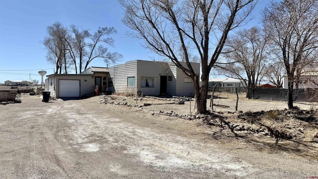 view of front facade with a garage, dirt driveway, and fence