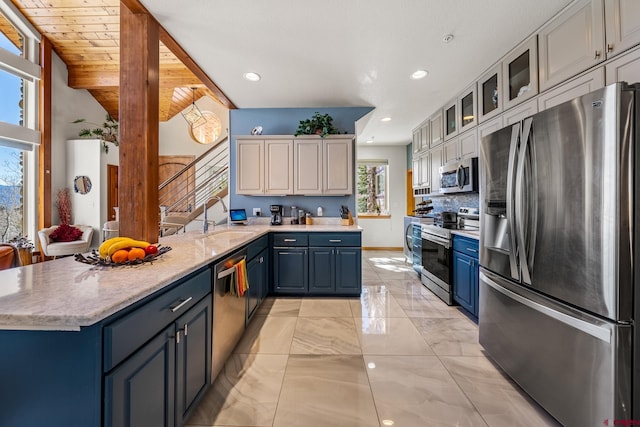 kitchen with blue cabinetry, decorative backsplash, a peninsula, stainless steel appliances, and a sink