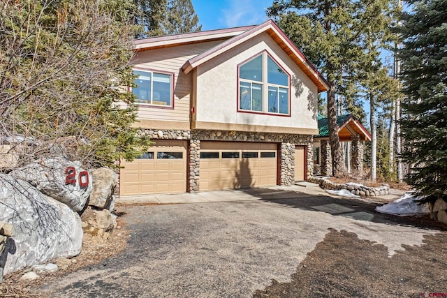 view of front of home featuring an attached garage, stone siding, driveway, and stucco siding