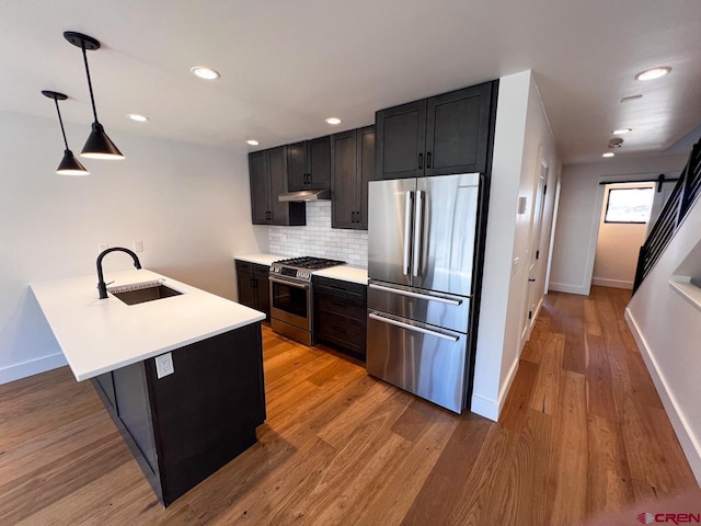 kitchen featuring a sink, backsplash, a barn door, appliances with stainless steel finishes, and light wood finished floors