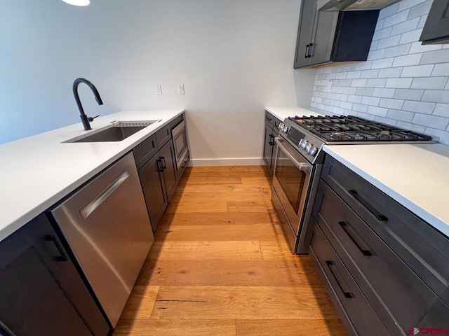 kitchen with light wood-style flooring, a sink, decorative backsplash, light countertops, and appliances with stainless steel finishes