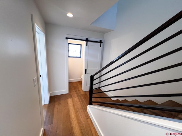 staircase with recessed lighting, a barn door, baseboards, and wood finished floors