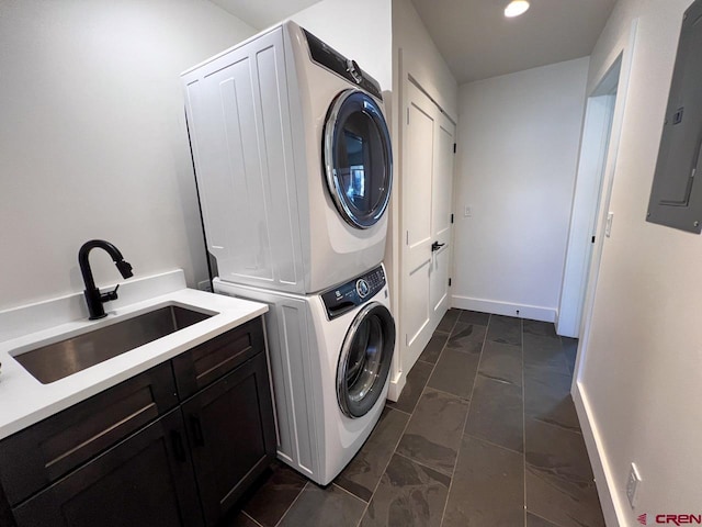 laundry area featuring baseboards, stacked washer and dryer, electric panel, cabinet space, and a sink