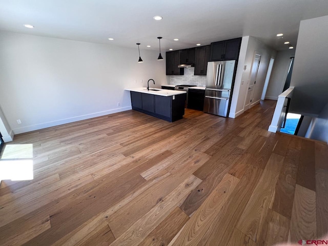 kitchen featuring light countertops, a peninsula, freestanding refrigerator, wood finished floors, and a sink