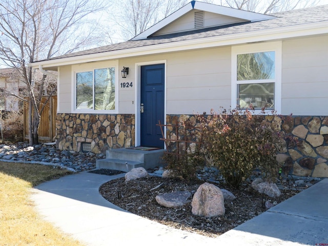 doorway to property with crawl space, stone siding, fence, and a shingled roof