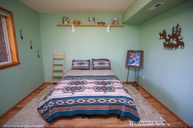 bedroom with wood finished floors, visible vents, and baseboards