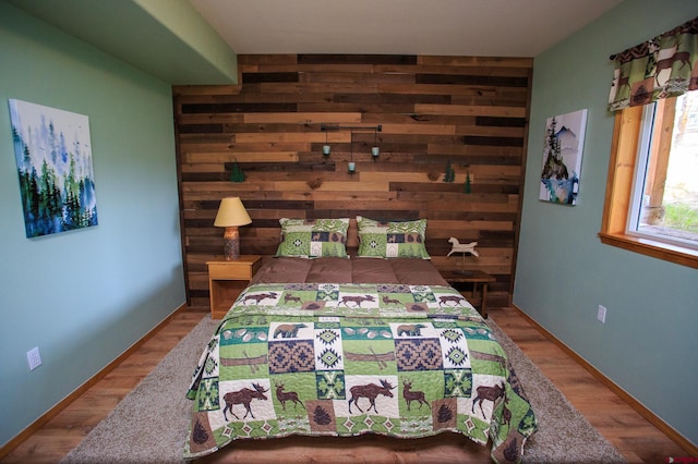 bedroom featuring an accent wall, wooden walls, wood finished floors, and baseboards