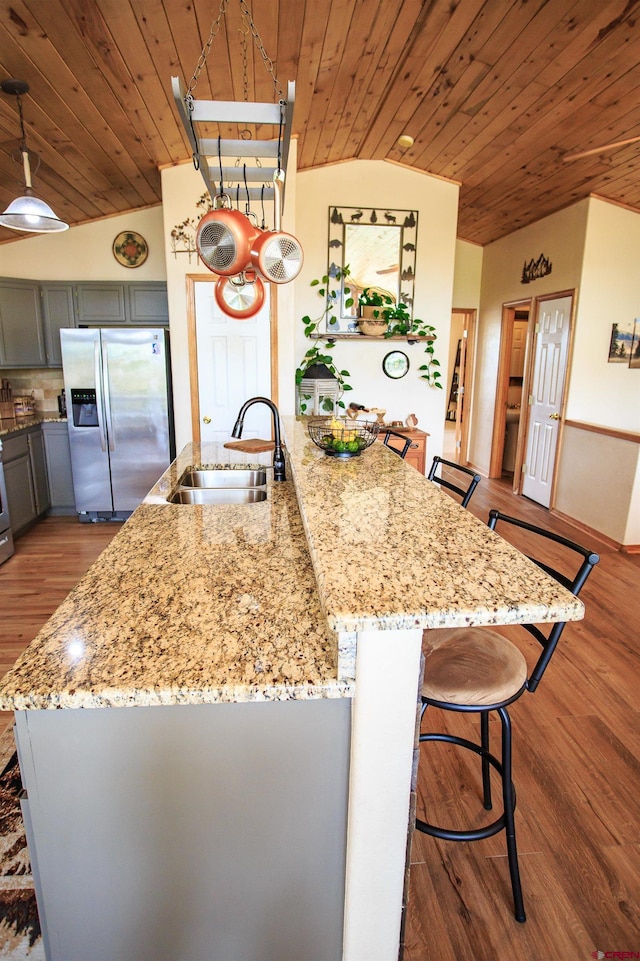 kitchen with light stone counters, gray cabinets, a sink, wood ceiling, and stainless steel fridge