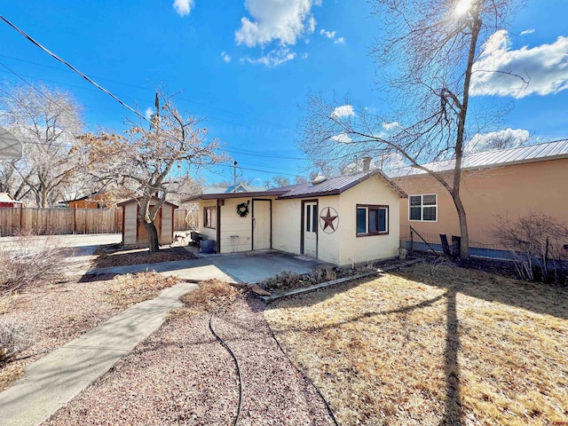 back of property with fence, stucco siding, an outdoor structure, a patio area, and metal roof