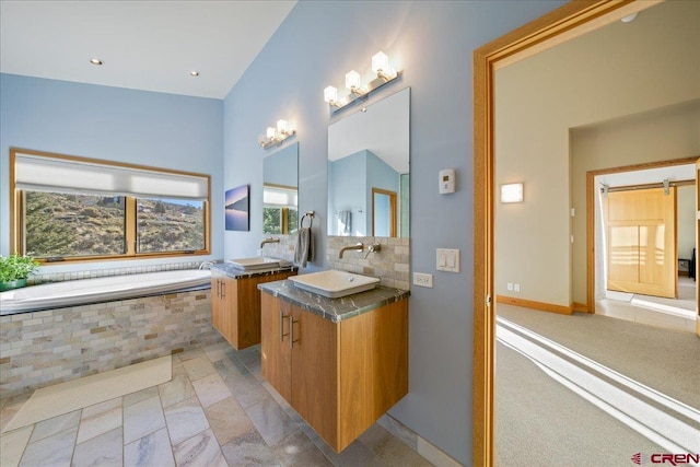full bathroom with baseboards, two vanities, a sink, decorative backsplash, and a garden tub