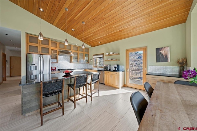kitchen featuring a breakfast bar, under cabinet range hood, glass insert cabinets, appliances with stainless steel finishes, and decorative backsplash
