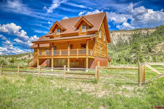 view of front of house featuring log exterior, fence, a forest view, and a shingled roof