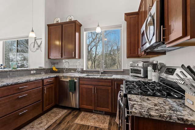 kitchen featuring dark wood-style floors, appliances with stainless steel finishes, dark stone counters, and a sink