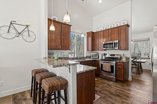 kitchen featuring light stone countertops, a peninsula, a sink, stainless steel appliances, and a kitchen breakfast bar