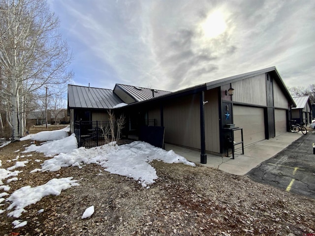 view of snow covered exterior featuring a standing seam roof, a garage, and metal roof