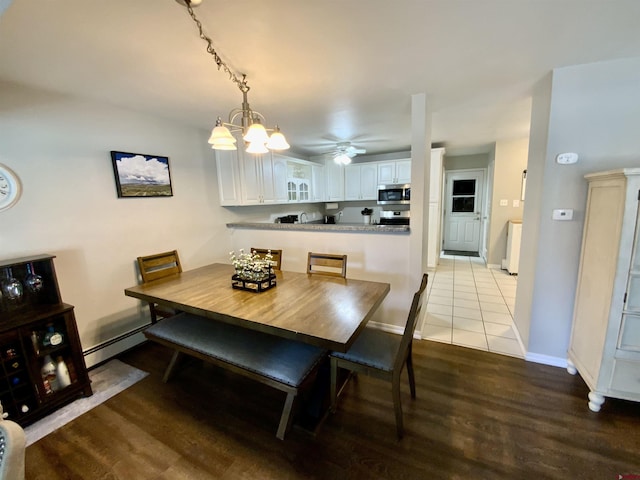 dining space with a baseboard radiator, baseboards, wood finished floors, and ceiling fan with notable chandelier