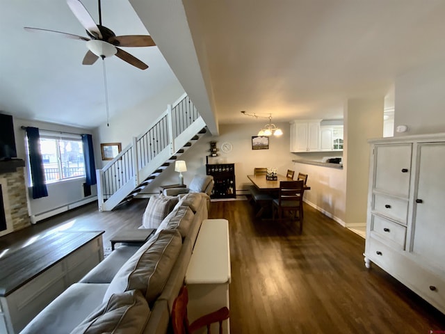 living room featuring baseboard heating, dark wood-style flooring, stairs, and ceiling fan with notable chandelier