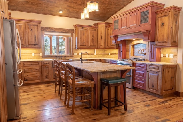 kitchen featuring light stone countertops, vaulted ceiling, light wood-style flooring, brown cabinets, and stainless steel appliances