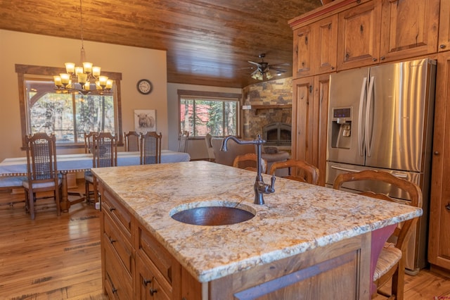 kitchen with wood ceiling, light stone counters, a fireplace, stainless steel refrigerator with ice dispenser, and a sink