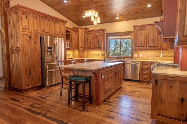 kitchen with a sink, stainless steel appliances, brown cabinetry, and vaulted ceiling