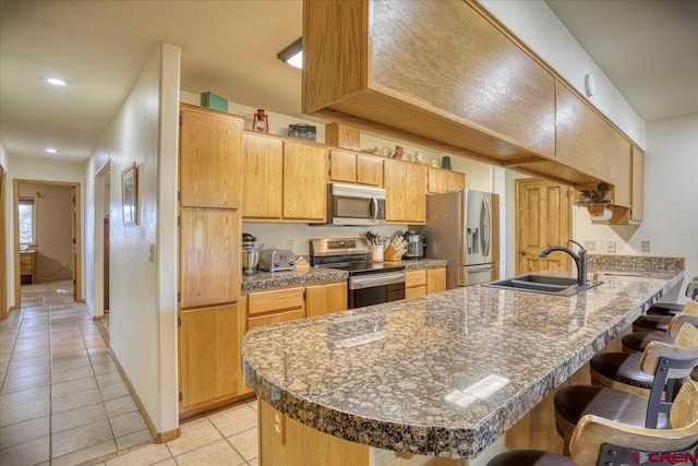 kitchen with a sink, appliances with stainless steel finishes, a breakfast bar area, a peninsula, and light tile patterned floors