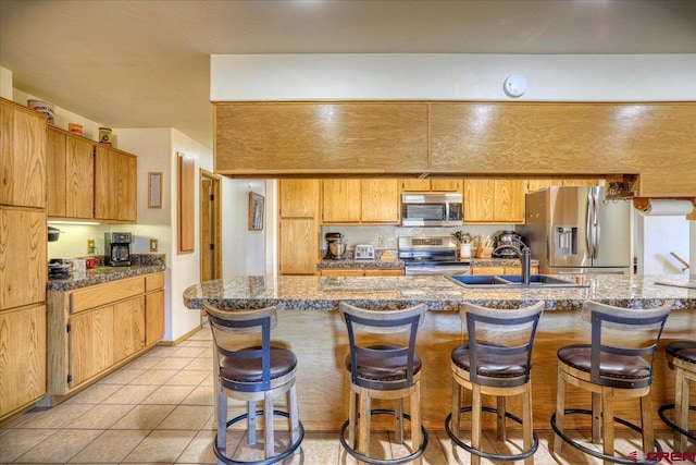 kitchen featuring light tile patterned flooring, appliances with stainless steel finishes, a breakfast bar, and a sink