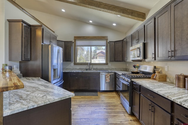 kitchen with dark brown cabinetry, lofted ceiling with beams, light stone counters, stainless steel appliances, and a sink