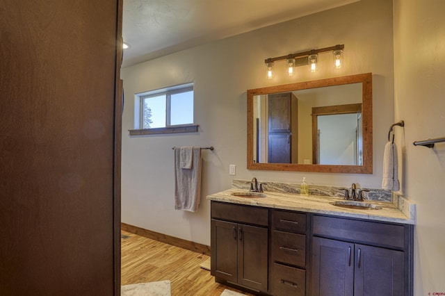 full bathroom featuring double vanity, wood finished floors, baseboards, and a sink