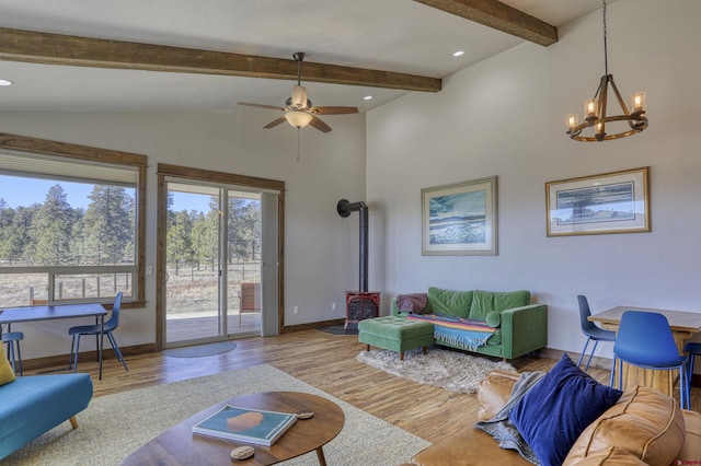 living room featuring a wood stove, ceiling fan with notable chandelier, wood finished floors, baseboards, and vaulted ceiling with beams